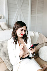 Young woman in a white suit, skirt in the house sitting on the floor near the bed talking on the phone communication with colleagues friends Internet