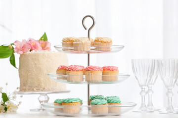 Dessert stands with tasty cupcakes and glasses on table