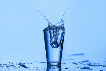 Glass of water with splash on color background