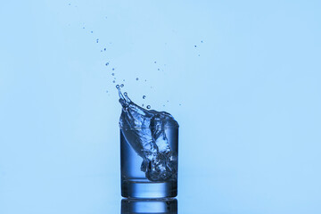 Glass of water with splash on color background
