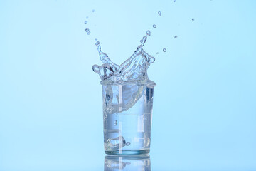 Glass of water with splash on color background