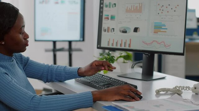 Black disabled handicapped businesswoman immobilized in wheelchair working at financial project typing on computer showing data prosessing on display sitting in start up business office