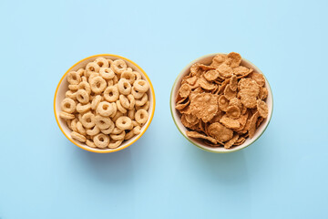 Bowls with tasty corn flakes and cereal rings on color background