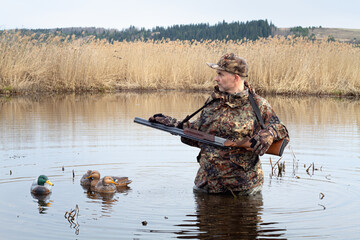 hunter stands in the middle of the lake next to plastic duck decoys