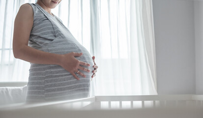 Happy Smiling Asian Pregnant female standing touching her belly in bedroom at home. Woman relaxing...