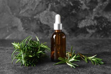 Bottle of essential oil and fresh rosemary on dark background