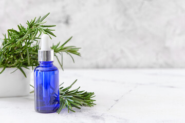 Bottle of essential oil and fresh rosemary on light background