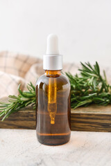 Bottle of essential oil and fresh rosemary on light background