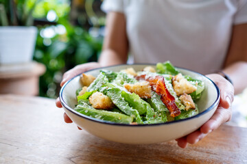 Closeup image of a woman holding and eating a Caesar salad