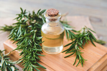 Bottle of essential oil and fresh rosemary on wooden background, closeup