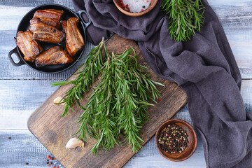 Composition with fresh rosemary, spices and grilled ribs on light wooden background