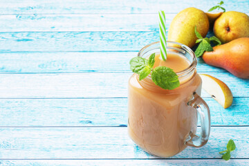 Natural pear juice in a glass cup. Juicy ripe conferences pears and mint leaves. top view copy space Bright blue background.