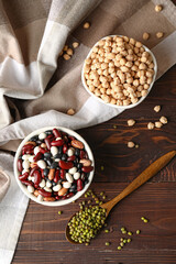 Bowls and spoon with different legumes on wooden background