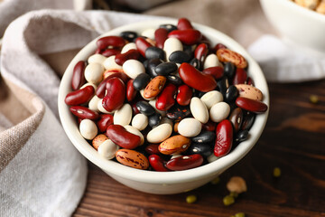 Bowl with different legumes on wooden background, closeup