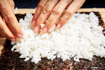 Female chef preparing rice on nori for delicious sushi. Asian food concept