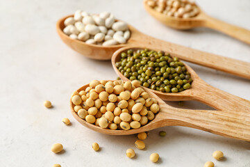 Spoons with different legumes on light background, closeup