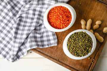 Bowls with different lentils and peanuts on light wooden background