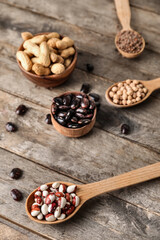 Bowls and spoons with different legumes on wooden background