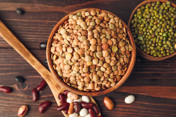 Bowls and spoon with different legumes on wooden background