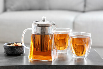 Teapot and cups of hot beverage on table in room