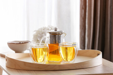 Teapot and glasses with hot beverage on tray in room