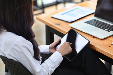 Rear view of woman office worker sitting at office desk and using digital tablet.