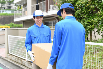 屋外で作業服を着た複数の男性が引っ越しの段ボールを運ぶイメージ