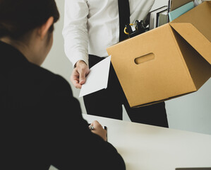Desperately fired man office worker employee hands her employer her resignation letter and packs her belongings in a cardboard box concept dismissal and unemployment