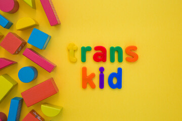 Transgender or cisgender LGBTQ plus pride concept. Different colourful plastic letters make the word Trans boy kid on the bright yellow background. Defining yourself, be proud of who you are