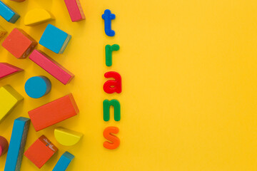 Transgender or cisgender LGBTQ plus pride concept. Different colourful plastic letters make the word Trans man boy kid on the bright yellow background. Defining yourself, be proud of who you are
