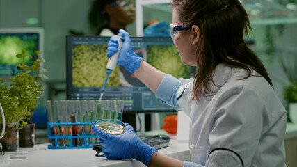 Scientist woman taking genetic solution from test tube with micropipette putting in petri dish...