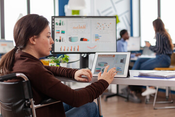 Multitasking paralyzed project manager, businesswoman with disabilites invalid immobilized woman using computer and tablet in same time working in business start-up office sitting in wheelchair.