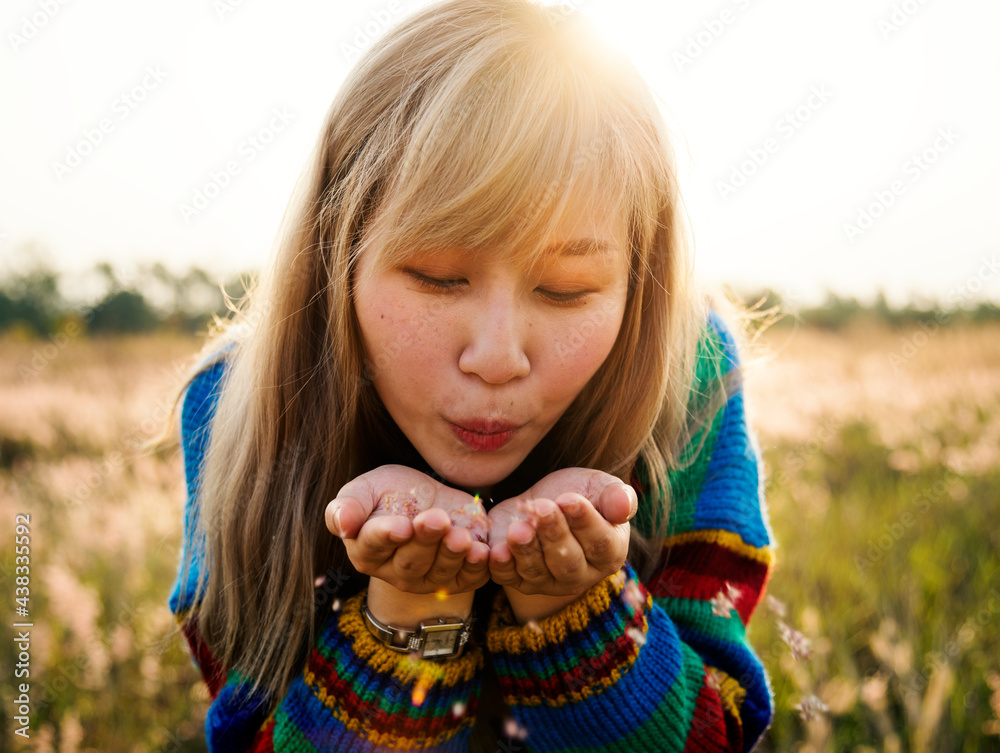 Wall mural asian woman blowing flower petals off her hands