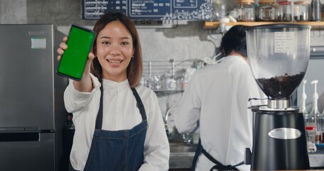 Asian happy beautiful young woman standing behind the bar counter in cafe smiling showing...