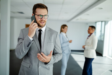 Young smiling businessman having phone call while standing in hallway before meeting.