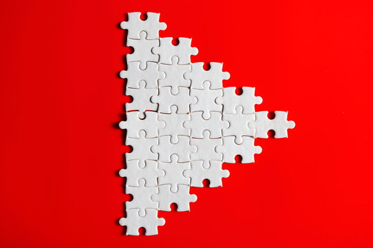 white jigsaw puzzle resemble small  triangle or play logo icon button on plain red background  