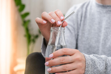 Young millennial blonde woman drinking water from eco bottle with metal reusable straw tube and doing yoga exercise stretching fitness at balcony home. Mindfulness meditation. 