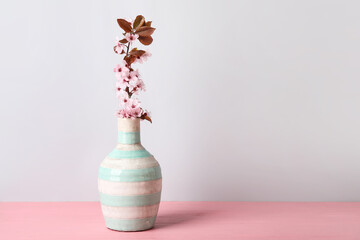 Vase with beautiful blossoming branch on table against light background