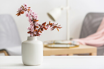 Vase with beautiful blossoming branches on table in room