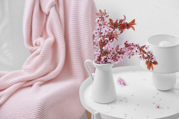 Jug with beautiful blossoming branches on table in room