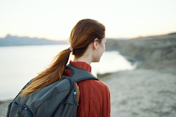 red-haired woman with a backpack on her back walks in nature in the mountains with a backpack on her back