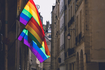 Two Lgbtq flags hanging at antique building corner during Paris pride. LGBTQIA culture symbol. Bright gay flags waving in wind at sunny day in Paris, France