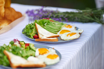 Selective focus of fresh appetizers for two and aromatic lavender bouquet. Close up view of beautiful table decoration outdoors, fresh salad with eggs and toasts. Concept of cuisine, food.