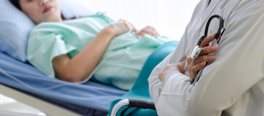 Doctor holding stethoscope and sitting in front of sick woman patient bed in hospital room.