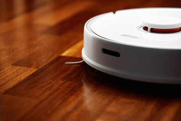 Smart Robot Vacuum Cleaner on wood floor. Robot vacuum cleaner performs automatic cleaning of the...