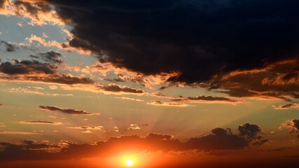 Shiny golden sun rays break through dark clouds. Orange color cloudscape of sunset. Dramatic sky while sundown in dusk
