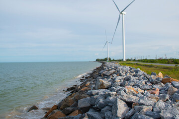 Stone dam to prevent beach waves, near wind turbines to generate electricity.