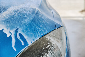 Car washing. Soap water running off from a washed blue car. Cleaning car with contactless high pressure washing