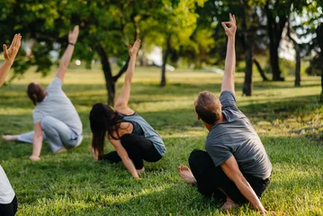 Fototapeten Eine Gruppe von Menschen macht bei Sonnenuntergang Yoga im Park. Gesunder Lebensstil, Meditation und Wellness © Andrii