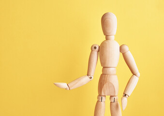 Wooden doll with gesture on yellow background. Mannequin shows gesture. Figure of wooden human with...